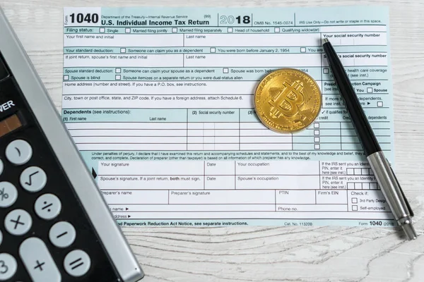 The pen, bitcoins and calculator on the tax form 1040 U.S. Individual Income Tax Return. The time to pay taxes