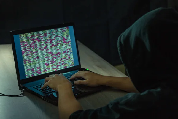 Хакер с капюшоном, использующий ноутбук для взлома систем — стоковое фото