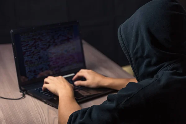 Hooded hacker using laptop to break systems — Stock Photo, Image