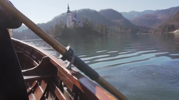 Detailní zpomalené pádla veslování v lodi na jezeře Bled s ostrov Bled a církve za ním a reflexe v jezeře, s sunflare na lodi — Stock video