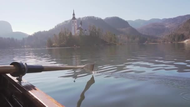 Wiosła w wodzie w słoneczny dzień - Wiosłowanie łodzią z wyspy jeziora Bled w tle - jezioro Bled, Słowenia — Wideo stockowe