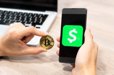 Nakit App logo Bitcoin sikke ve bilgisayar dizüstü - Slovenya 13.02.2019 yanında insan eli tarafından tutulan smartphone üzerinde görüntülenen kare Inc tarafından