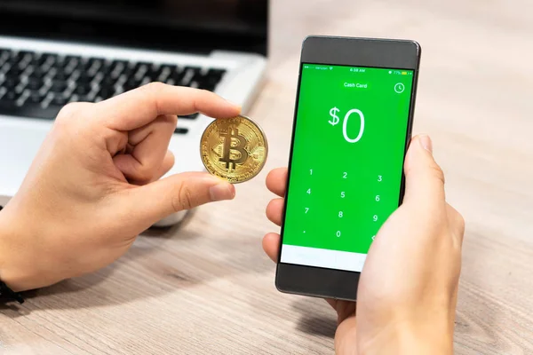 Készpénz App jelenik meg a smartphone mellett Bitcoin érme- és számítógép-laptop - Szlovénia 13.02.2019 emberi kéz birtokában tér Inc — Stock Fotó