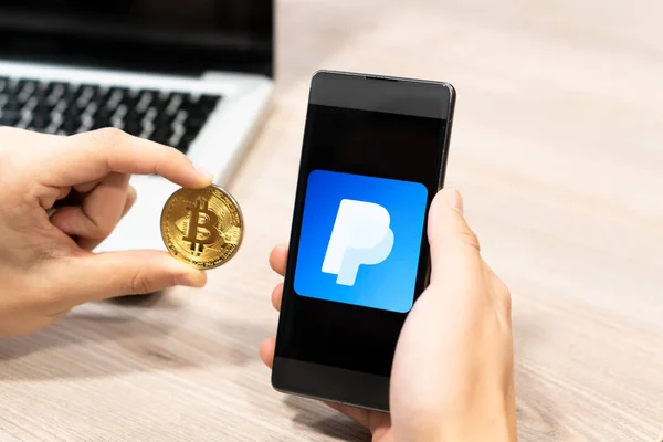 Cep telefonu ve Bitcoin para - paypal logosu göstermek üstünde telefon,, bilgisayar dizüstü arka planda tutan eller. Slovenya 13.02.2019
