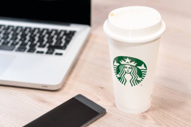 Starbucks kahve Kupası ahşap masa ofis bilgisayar dizüstü bilgisayar ve cep telefonu yanında. Slovenya 13.02.2019