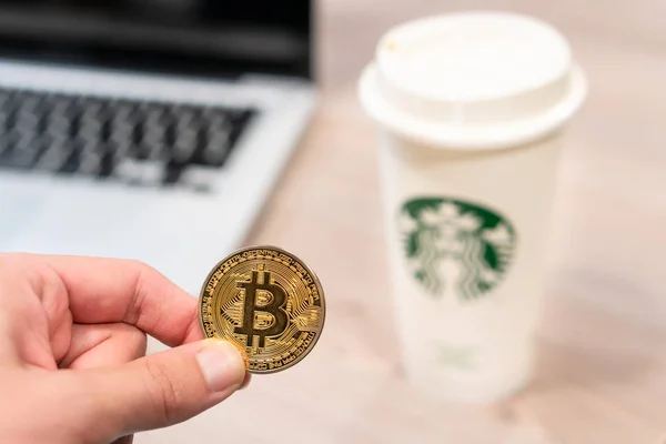 Kryptowährung Bitcoin neben Starbucks-Kaffeetasse. — Stockbild Kryptowährung Bitcoin, gehalten von einer humorvollen Hand neben einer Starbucks-Kaffeetasse. Slowenien 13.02.2019 — Stockfoto