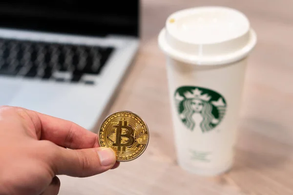 Kryptowährung Bitcoin neben Starbucks-Kaffeetasse. — Stockbild Kryptowährung Bitcoin, gehalten von einer humorvollen Hand neben einer Starbucks-Kaffeetasse. Slowenien 13.02.2019 — Stockfoto