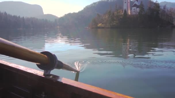 Une pagaie dans l'eau par une journée ensoleillée - Ramer le bateau avec l'île Lac de Bled dans le fond - Lac de Bled, Slovénie — Video