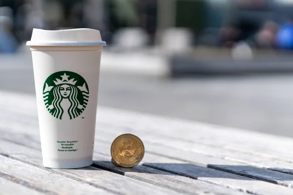 Cryptocurrency Bitcoin naast Starbucks cup. Starbucks aanname van concept van de blockchain - Slovenië - 28.2.2019 — Stockfoto