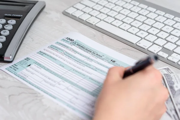 Foto de manos calculando y llenando el formulario de impuestos al lado del teclado de la computadora, billetes de dólar y formulario de impuestos 1040. 15 de abril 2019 día de impuestos — Foto de Stock