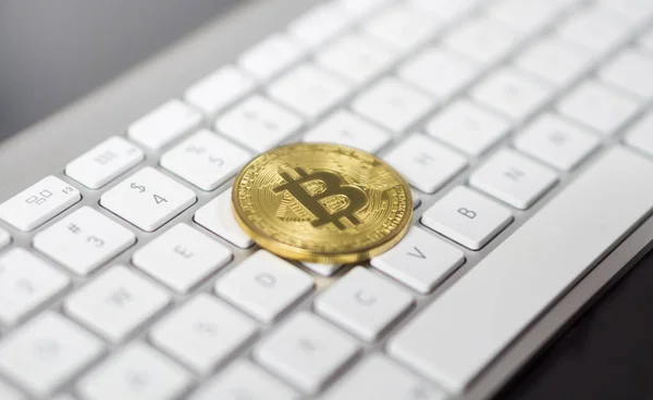 Die Kryptowährung Bitcoin liegt auf einer weißen Tastatur im Hintergrund. Symbol für elektronisches virtuelles Geld. — Stockfoto