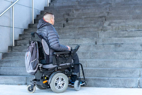 Jeune homme handicapé dans un fauteuil roulant électrique devant les escaliers — Photo