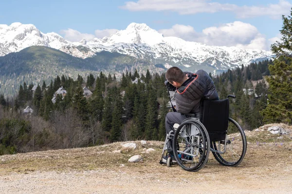 Hombre discapacitado en silla de ruedas usando la cámara en la naturaleza, fotografiando hermosas montañas —  Fotos de Stock