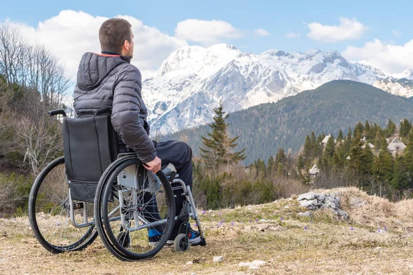 Junger behinderter Mann im Rollstuhl draußen in der Natur und beobachtet Berge und Natur — Stockfoto