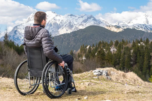 Junger behinderter Mann im Rollstuhl draußen in der Natur und beobachtet Berge und Natur — Stockfoto