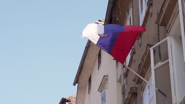 Drapeau national de la République de Slovénie contre le soleil et le ciel bleu agitant devant un appartement. Mouvement lent — Video