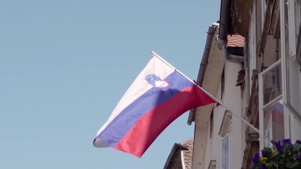 Bandera nacional de la República de Eslovenia contra el sol y el cielo azul ondeando fuera de un apartamento. Lento. — Vídeos de Stock