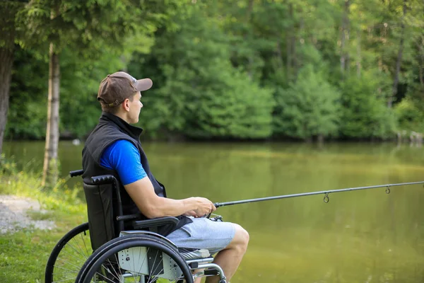 Engelli adam gölde tekerlekli sandalyede balık tutuyor — Stok fotoğraf