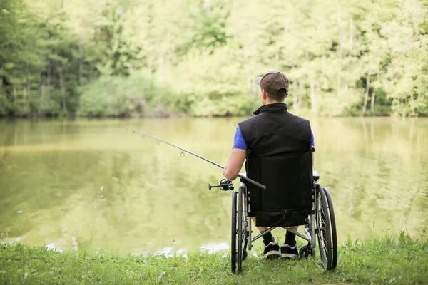 Hombre discapacitado en silla de ruedas pesca en el lago —  Fotos de Stock