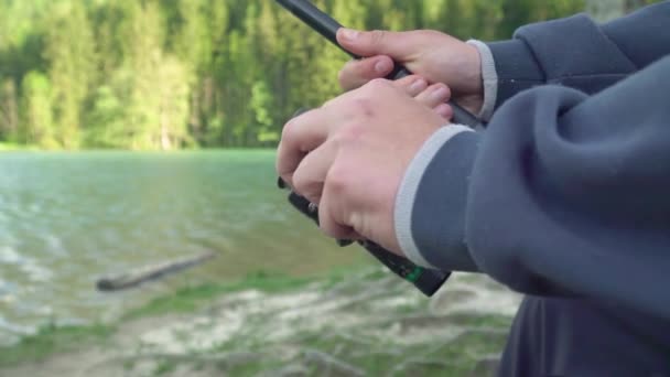 Cámara lenta primer plano de un hombre sosteniendo una caña de pescar y carrete o pescador en un día soleado cerca del lago . — Vídeos de Stock