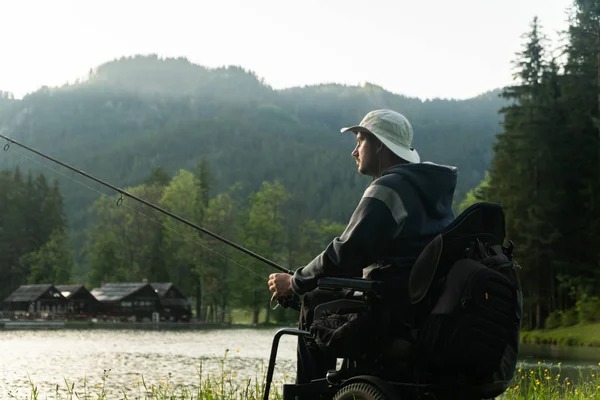 Young man in a wheelchair fishing at the beautiful lake in sunset, dawn — Stock Photo, Image