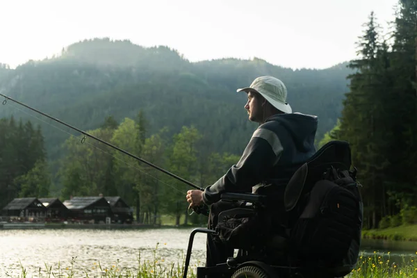 Junger Mann im Rollstuhl angelt am schönen See im Sonnenuntergang, im Morgengrauen — Stockfoto