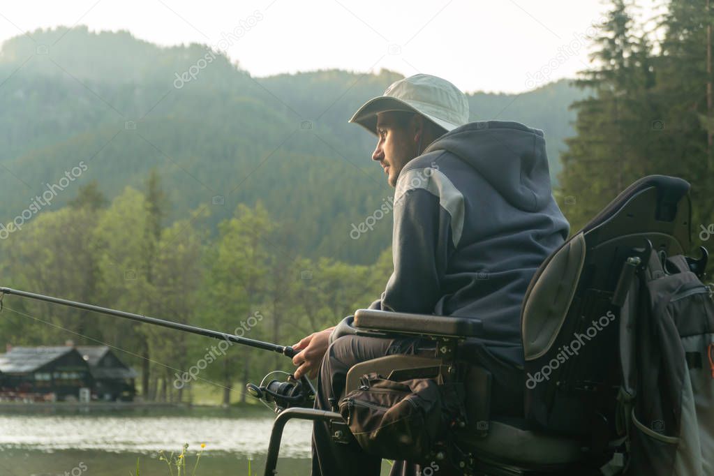 young man in a wheelchair fishing at the beautiful lake in sunset, dawn