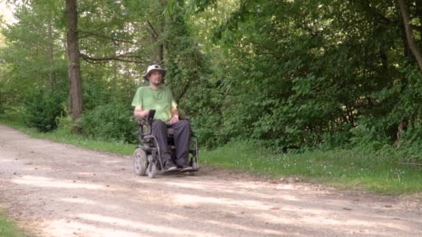 Slowmotion podąża za niepełnosprawnym młodym mężczyzną na wózku obserwując naturę wokół niego — Wideo stockowe