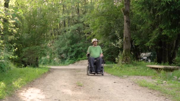 Retrato en cámara lenta del joven discapacitado en silla de ruedas observando la naturaleza a su alrededor, deteniéndose frente a la cámara — Vídeos de Stock