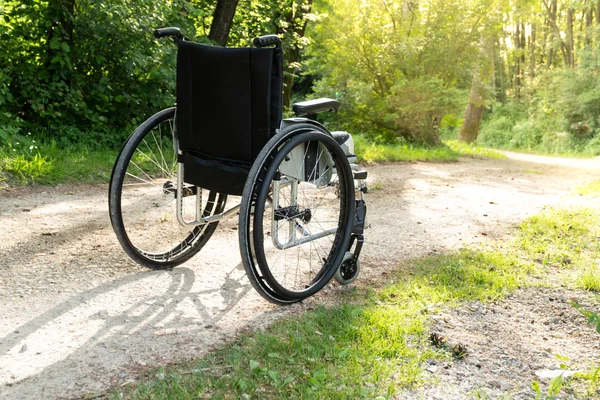 Empty wheelchair parked in park, health care concept, with sun flare — Stock Photo, Image