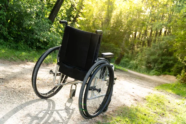 Empty wheelchair parked in park, health care concept with sun flare — Stock Photo, Image