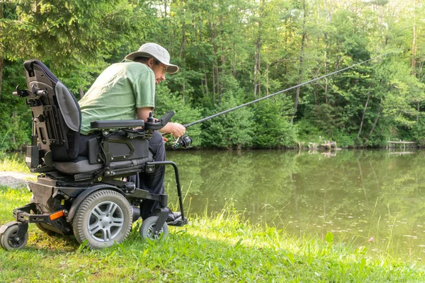 Hombre feliz en una silla de ruedas eléctrica esperando para coger un pez en el hermoso estanque en natue en un día soleado — Foto de Stock