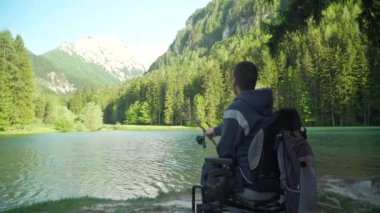 arka ormanda ve dağa yakın güzel bir gölde elektrikli tekerlekli sandalye balıkçılık içinde özürlü balıkçı 4k çözünürlüğü