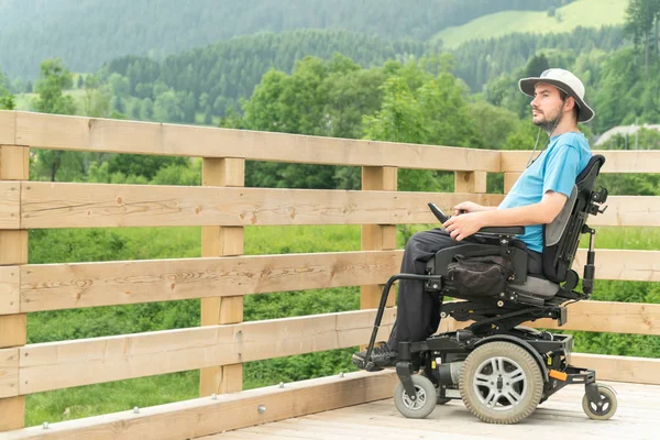 遊歩道で電動車椅子に乗った障害者の若者が自由を楽しみ、自然を観察する — ストック写真