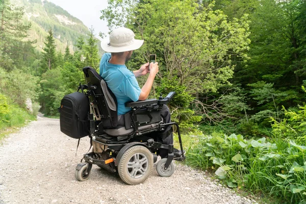 Mann im Elektrorollstuhl mit Smartphone-Kamera in der Natur — Stockfoto