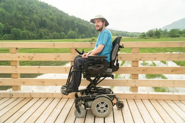 Discapacitado joven feliz en silla de ruedas eléctrica en un paseo marítimo disfrutando de su libertad y sonriendo — Foto de Stock