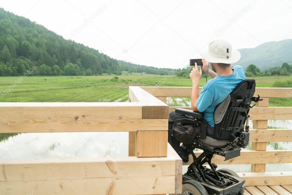 man on electric wheelchair using smartphone camera near the lake in nature