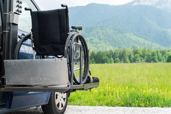 Black electric lift specialized vehicle for people with disabilities. Empty wheelchair on a ramp with nature and mountains in the back — Stock Photo, Image