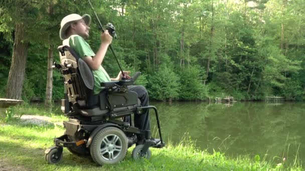 4k resolution of happy man in a electric wheelchair fishing at the beautiful pond in natue on a sunny day — Stock Video