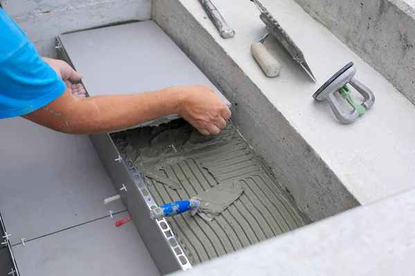 The hands of the tiler are laying the ceramic tile on the floor.