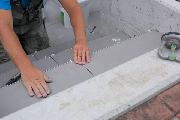 The hands of the tiler are laying the ceramic tile on the floor.