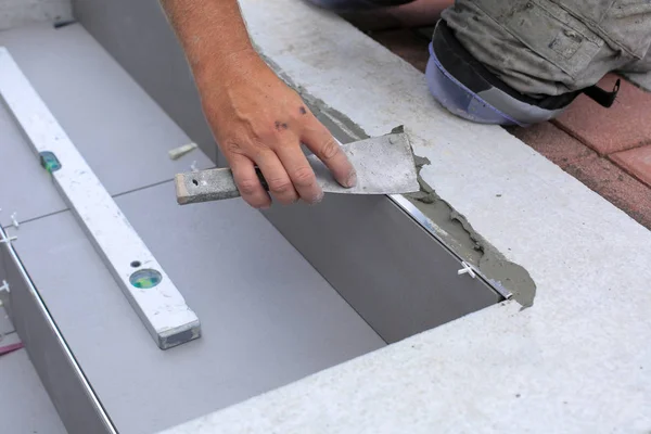 The hands of the tiler are laying the ceramic tile on the floor.