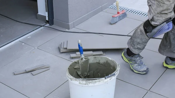 The hands of the tiler are laying the ceramic tile on the floor.