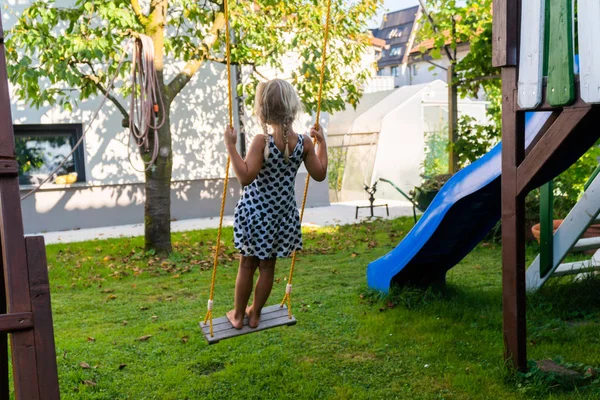 3-5 летняя блондинка развлекается на качелях на открытом воздухе. Летняя площадка. Девочка качается высоко. Маленький ребенок на качелях в саду — стоковое фото