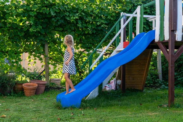 Счастливая молодая блондинка, играющая на красочной детской площадке. Детские игры в детском слайде — стоковое фото