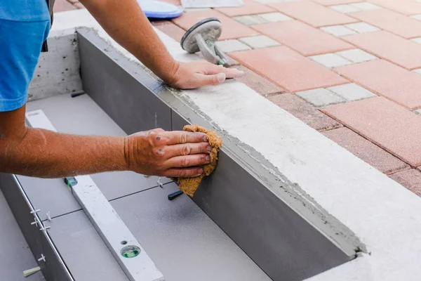 The hands of the tiler are laying the ceramic tile on the floor.