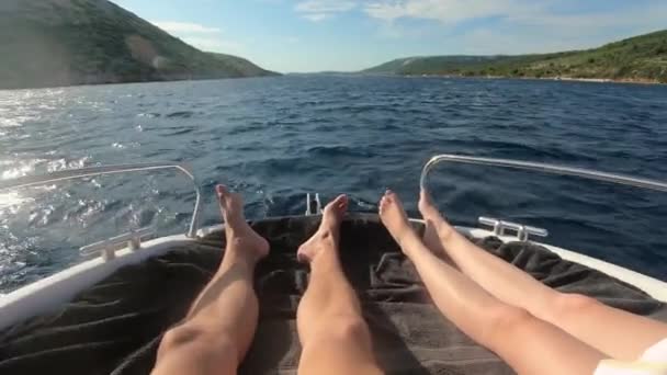 Vue sur les jambes de l'homme et de la femme allongées et conduisant sur un yacht avec une mer bleue tirquoise et une plage avec des palmiers verts en arrière-plan. concept vacances d'été de luxe . — Video