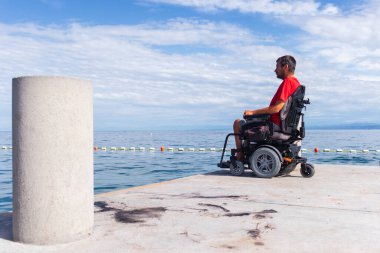 Sahilde tekerlekli sandalyede oturan adam.