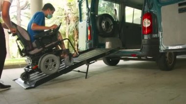 Tekerlekli sandalyedeki adam araç rampası kullanıyor.