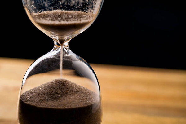 Running sand in the hourglass on table with black background, flowing time concept.